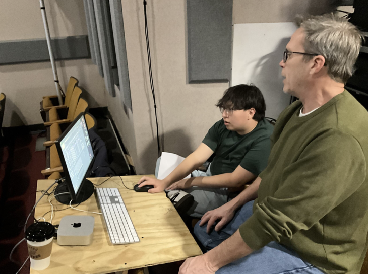 Associate Professor Michael Smith wearing a green sweater is working with Brandon Cericola at a computer.